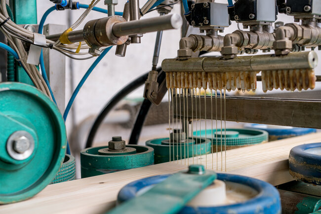 La colle thermofusible est appliquée mécaniquement sur une pièce de bois