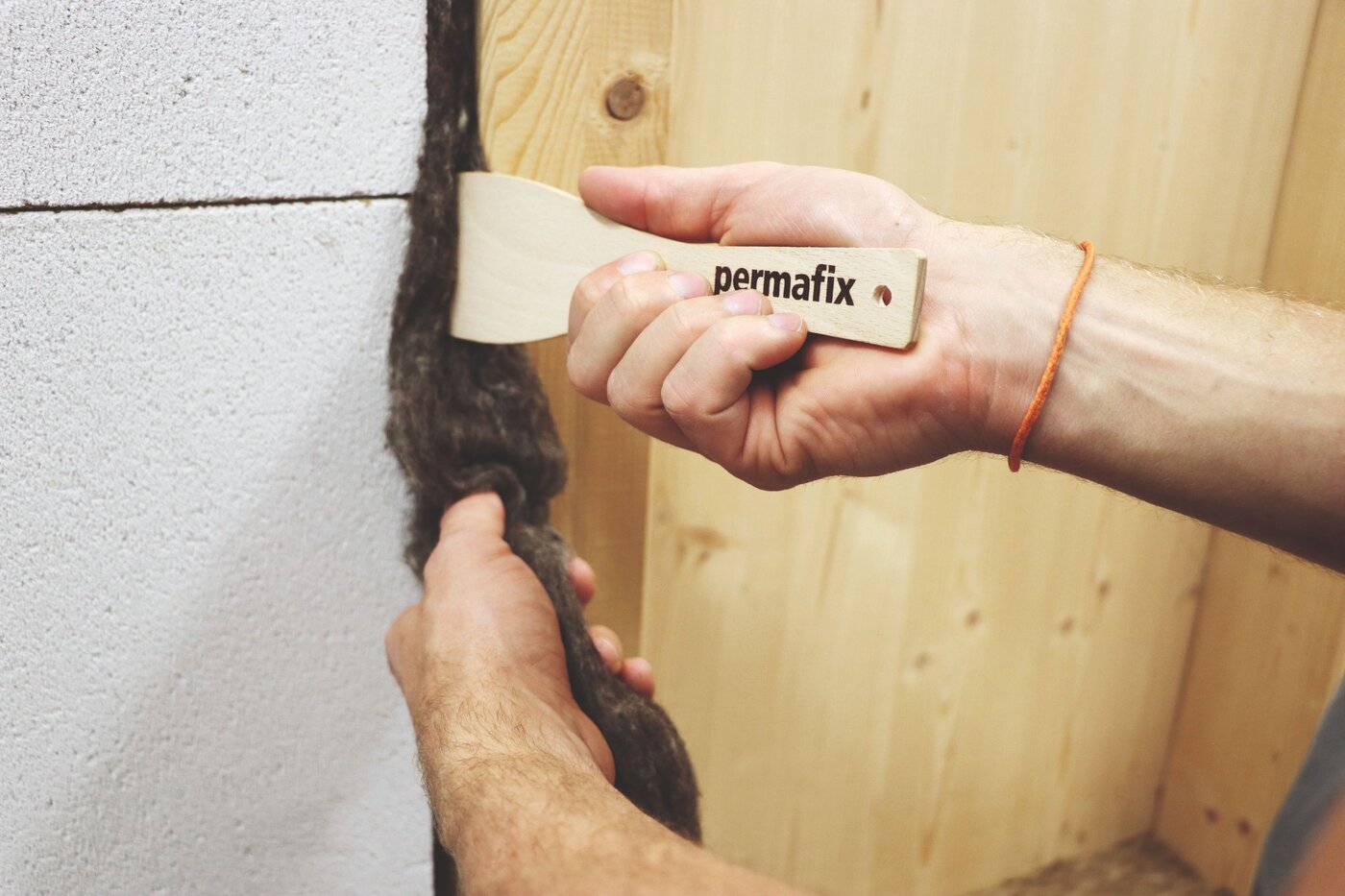 Un artisan bourre une tresse de joint Permafix 606 à l'aide d'une spatule dans un joint entre le béton et le bois