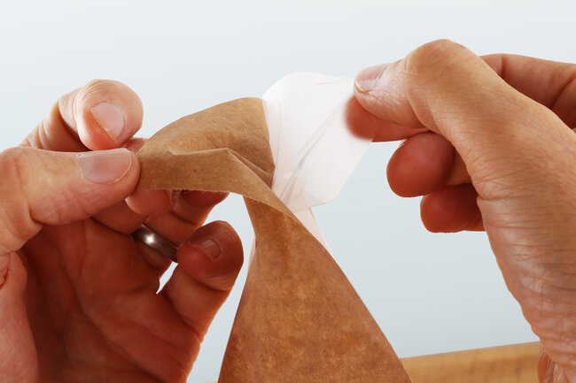 Deux mains séparent le papier et le film dans le cas d'un papier d'emballage séparable