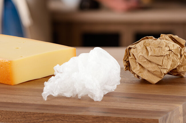 Un morceau de fromage sur un plateau de casse-croûte, à côté de papiers et de films plastiques froissés. 