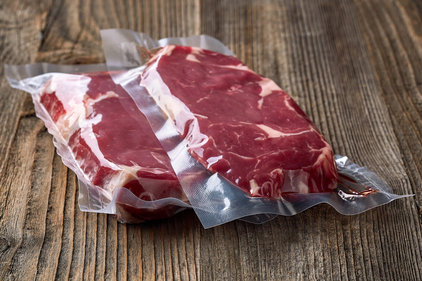 Deux steaks emballés sous vide sur une table en bois.