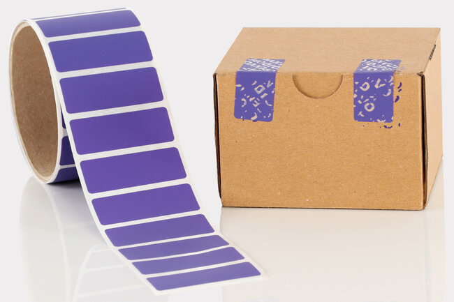 Rolle mit violetten VOID-Etiketten und ein kleiner Karton, der mit zwei VOID-Etiketten verschlossen ist