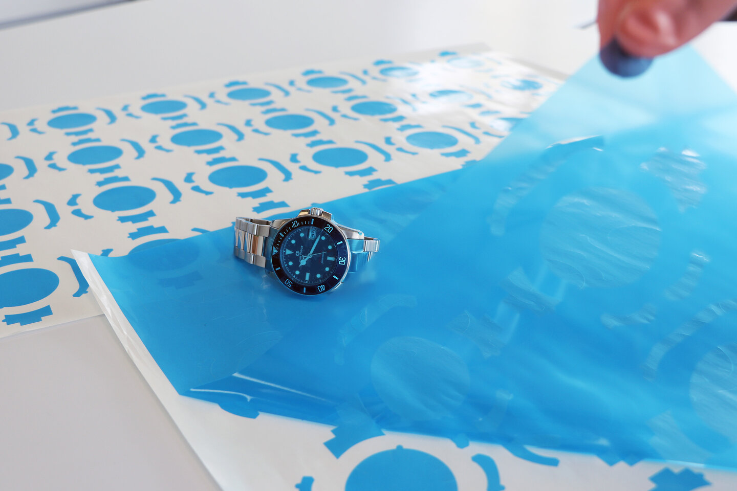 Von einem Bogen blauer Stanzteile wird das Stanzgitter abgezogen und eine Uhr liegt auf dem Bogen.