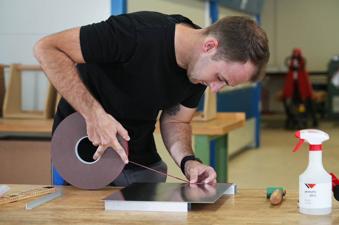 Le métallier applique un ruban adhésif de montage VST sur une plaque métallique.