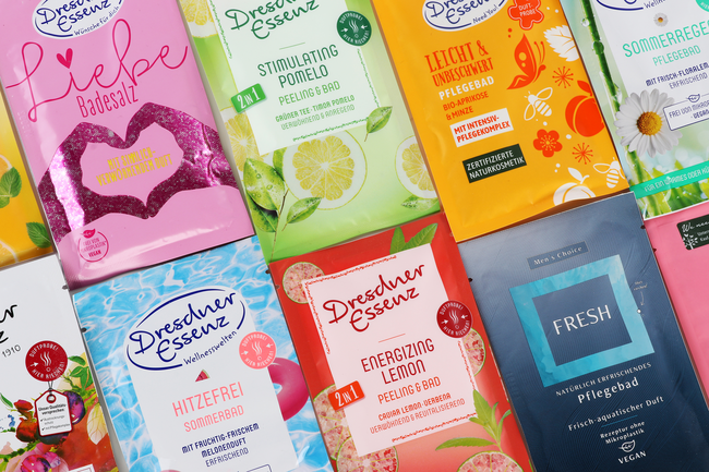 Plusieurs emballages en sachet pour produits de bain et de soin, de différentes couleurs et designs, disposés sur une surface plane