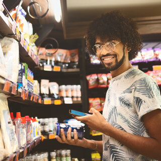 Un homme tient un produit et un téléphone portable dans les mains au rayon des produits de commodité.