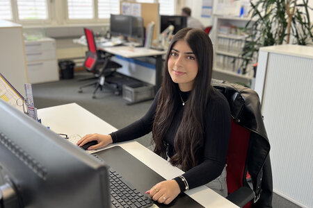 Une apprentie employée de commerce assise à son poste de travail devant son écran.