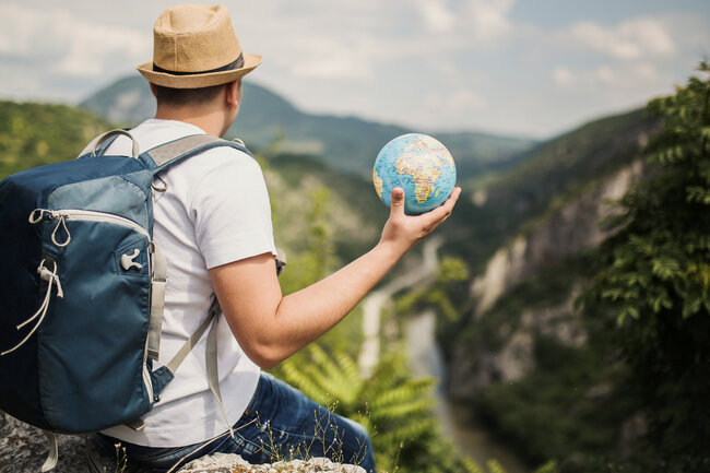 Un voyageur avec un sac à dos tient un globe et contemple un paysage montagneux