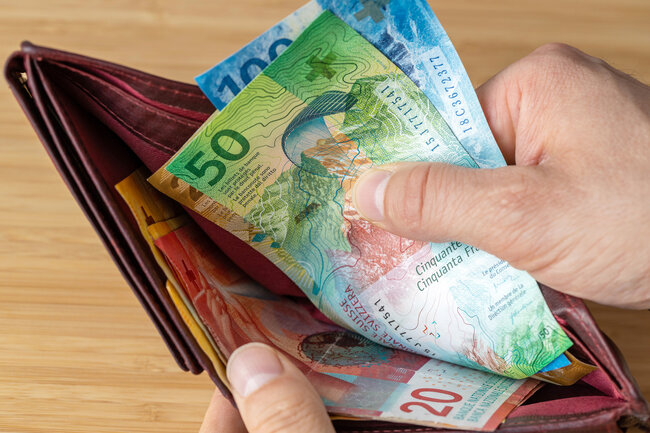 Une main retire des billets suisses d’un portefeuille.