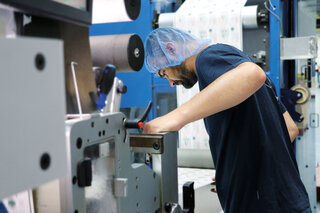 Mitarbeiter prüft an der Druckmaschine die Druckqualität von Etiketten.