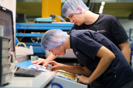 Deux apprentis imprimeurs d’emballages vérifient le résultat d’une impression à l’aide d’un compte-fils.