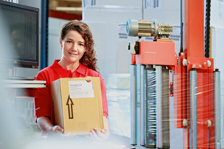 Une femme porte un carton avec une étiquette logistique.